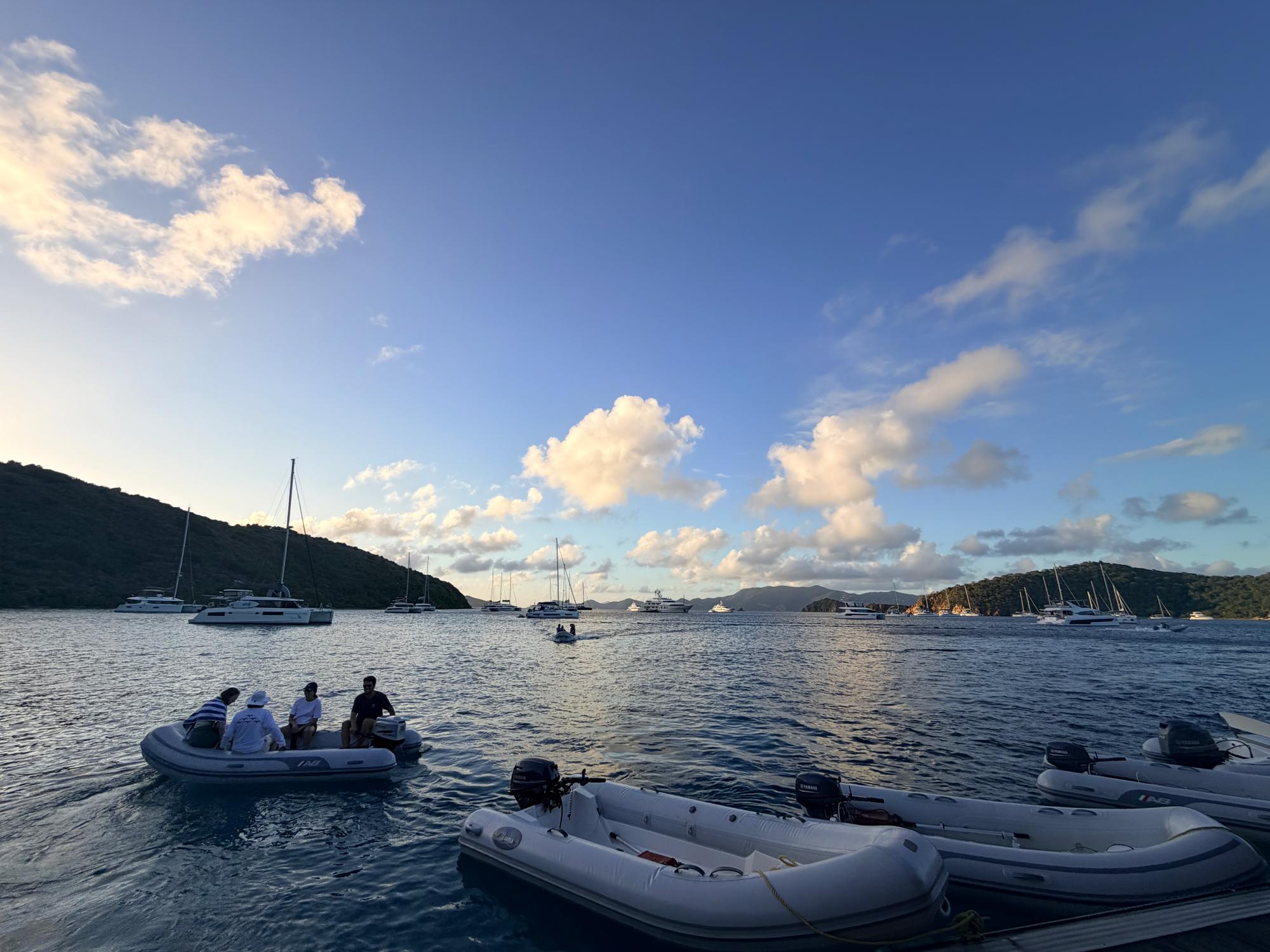 Crowded BVI anchorage at dusk during peak charter season, with dinghies running and boats rafted together.