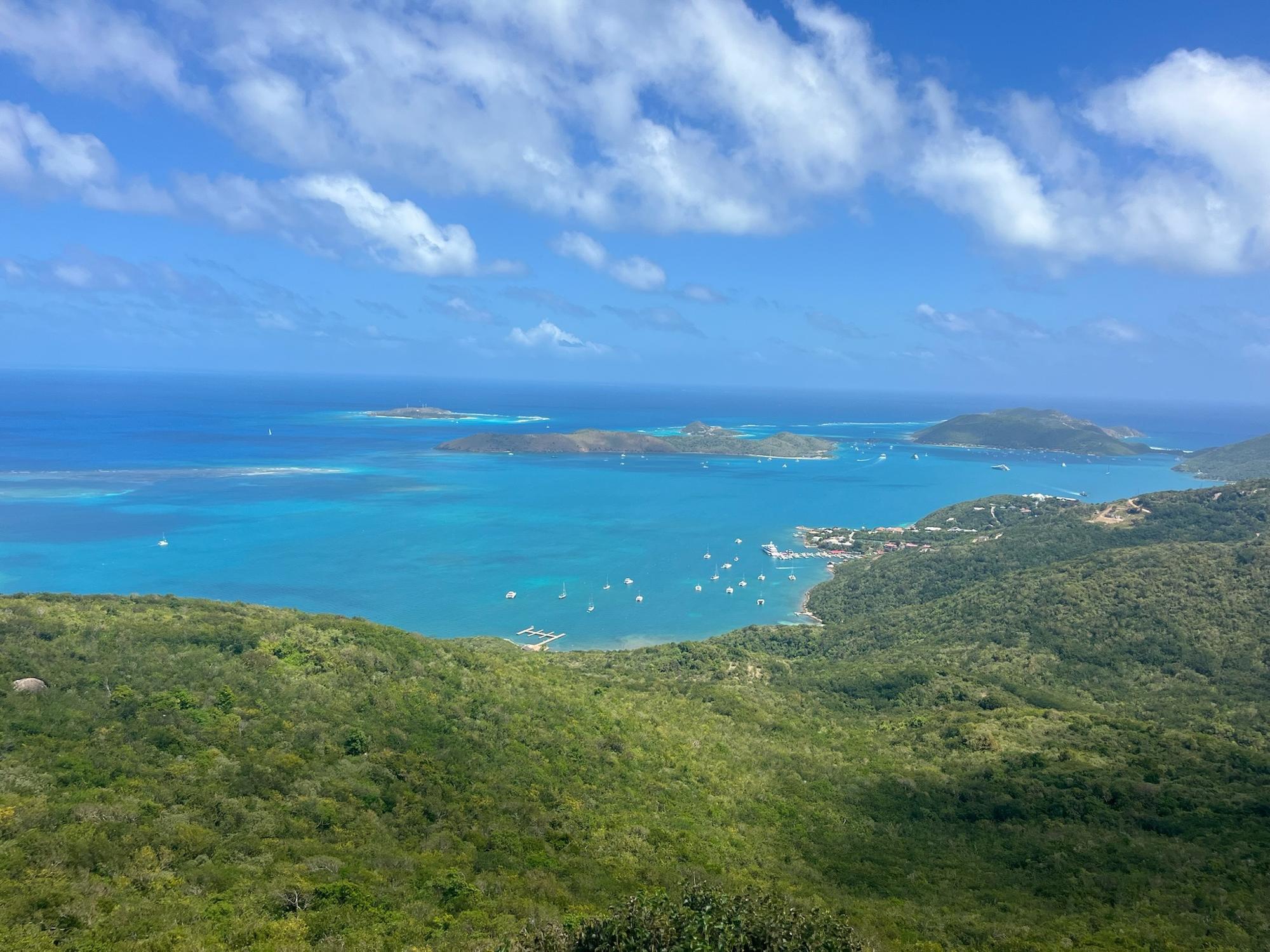 Aerial view of North Sound on Virgin Gorda, with sailboats anchored across turquoise Virgin Islands water and green hillside in the foreground.