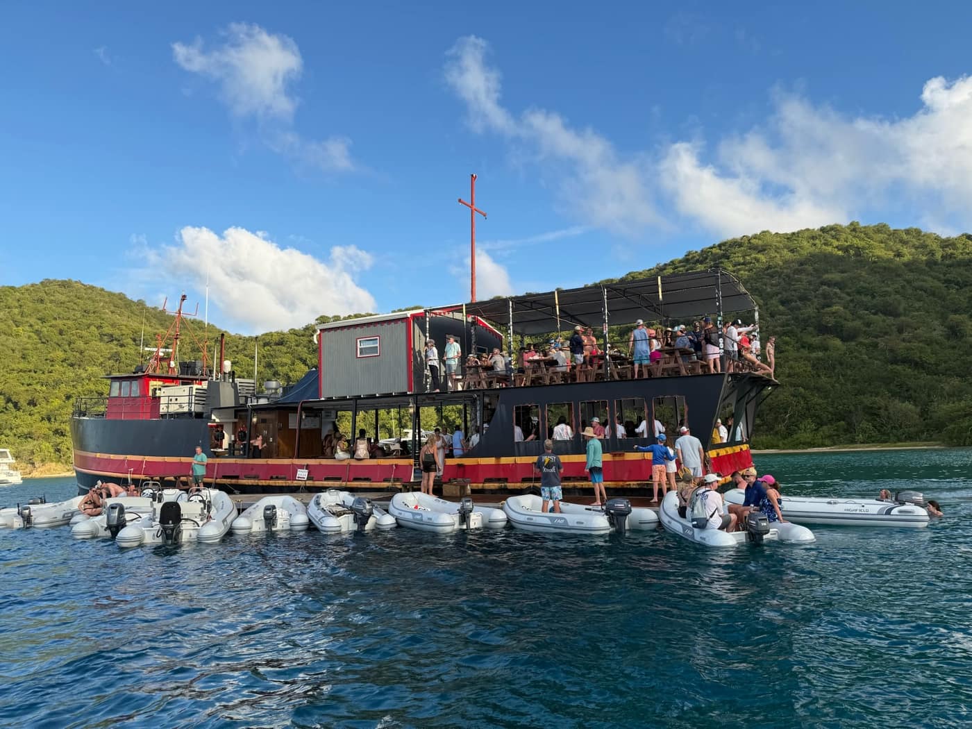 Willy T, the floating bar William Thornton, anchored in the Bight at Norman Island with dinghies rafted alongside and people on the top deck.