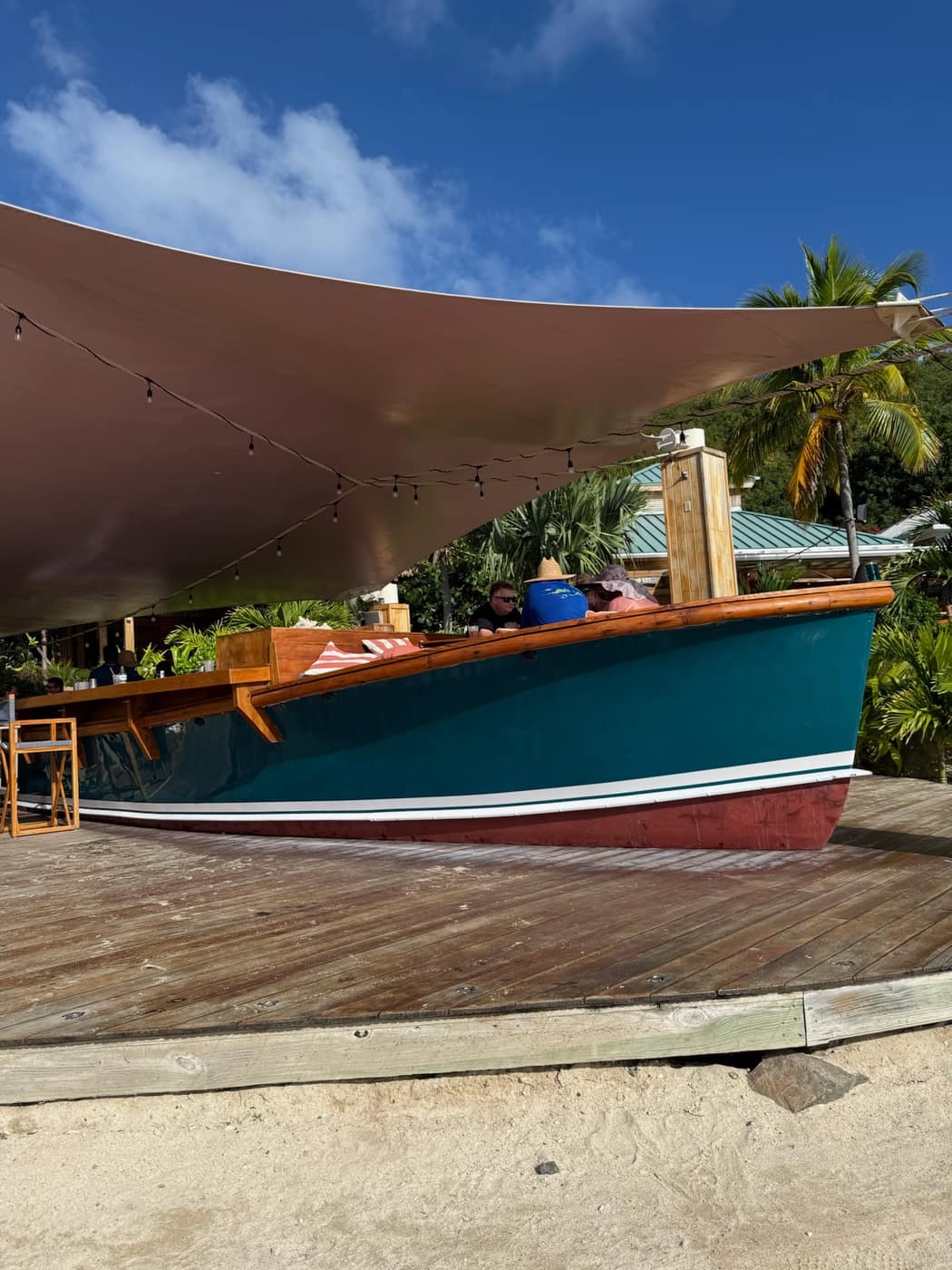 The Reef Sampler, a 1970s workboat refit as a floating bar at Bitter End Yacht Club, North Sound, with people seated along its rail under a shade sail.