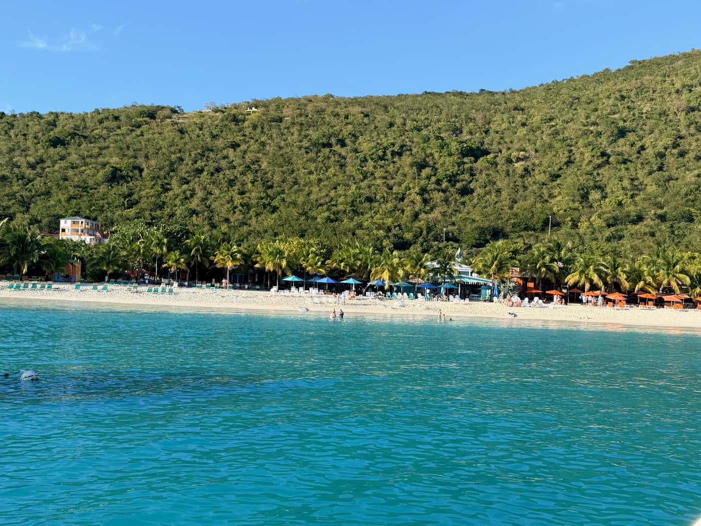 White Bay, Jost Van Dyke, seen from the water with Soggy Dollar and Hendo's Hideout's orange umbrellas along the beach and palm trees behind.