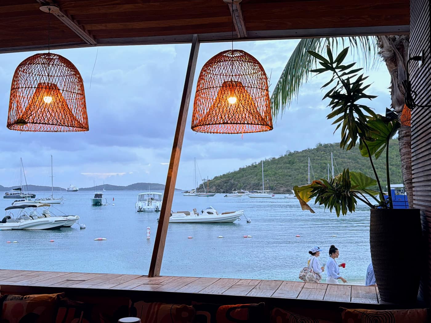 View from inside Karma restaurant, Cruz Bay, through woven pendant lamps and palm fronds, looking out over the harbor at dusk.