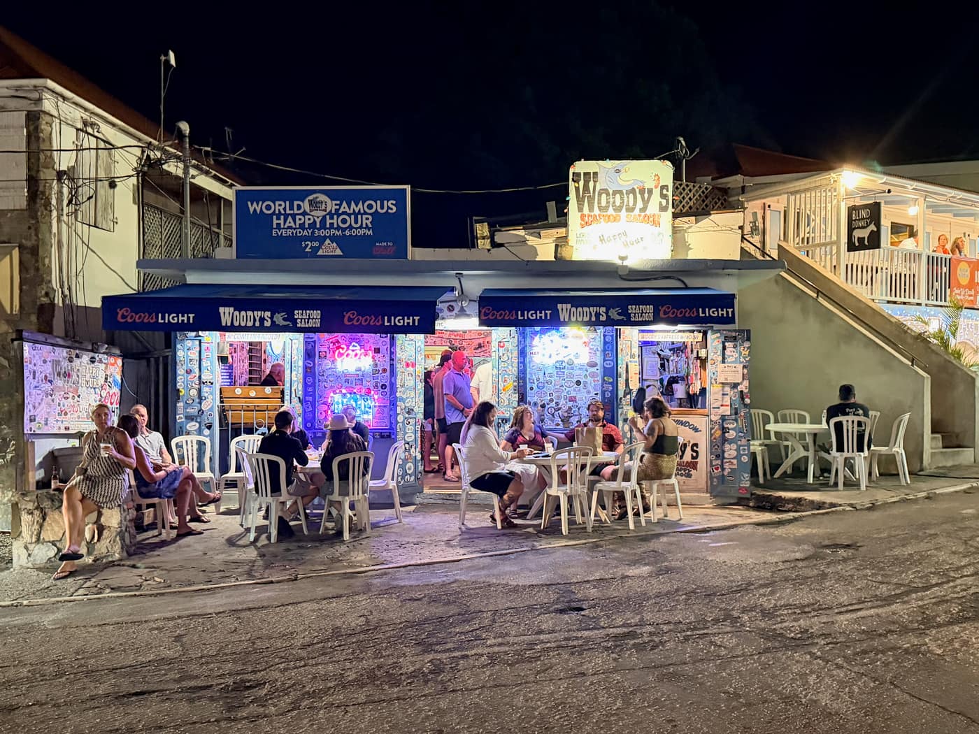 Woody's Seafood Saloon in Cruz Bay, St. John, lit up at night with tables of people out front and a happy hour sign overhead.