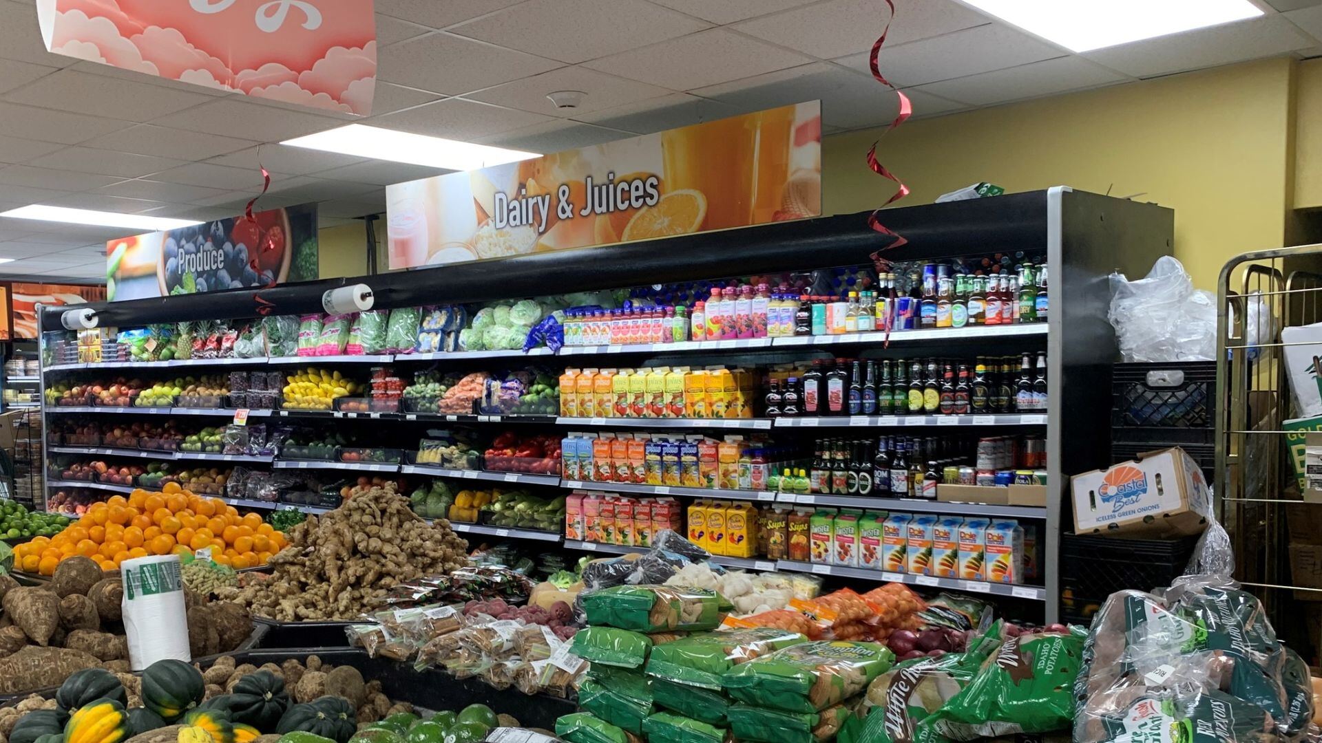 BVI supermarket interior showing the dairy and juices aisle with bottled drinks on the wall, produce wall with bagged vegetables and citrus in the foreground.